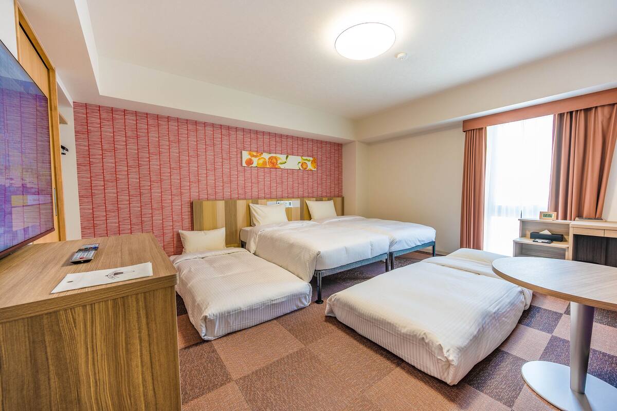 A hotel room with two beds, a desk, a TV, and a window with curtains.