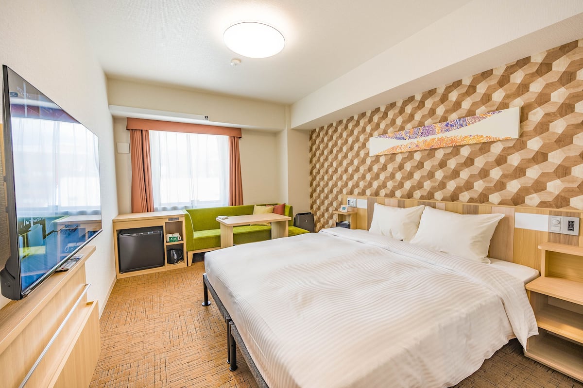 A hotel room with a large bed, a desk, a television, and a view of the city.