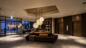 Un lobby moderno con un amplio sofá modular, iluminación colgante y vistas a la calle.