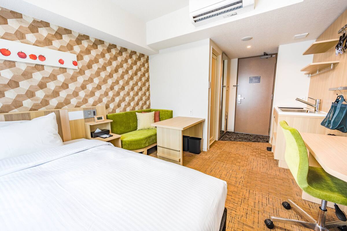 A hotel room with a bed, a green sofa, a desk, and a shower area.