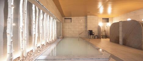 A modern indoor pool area with a clear glass wall, wooden ceiling, and tiled floor.