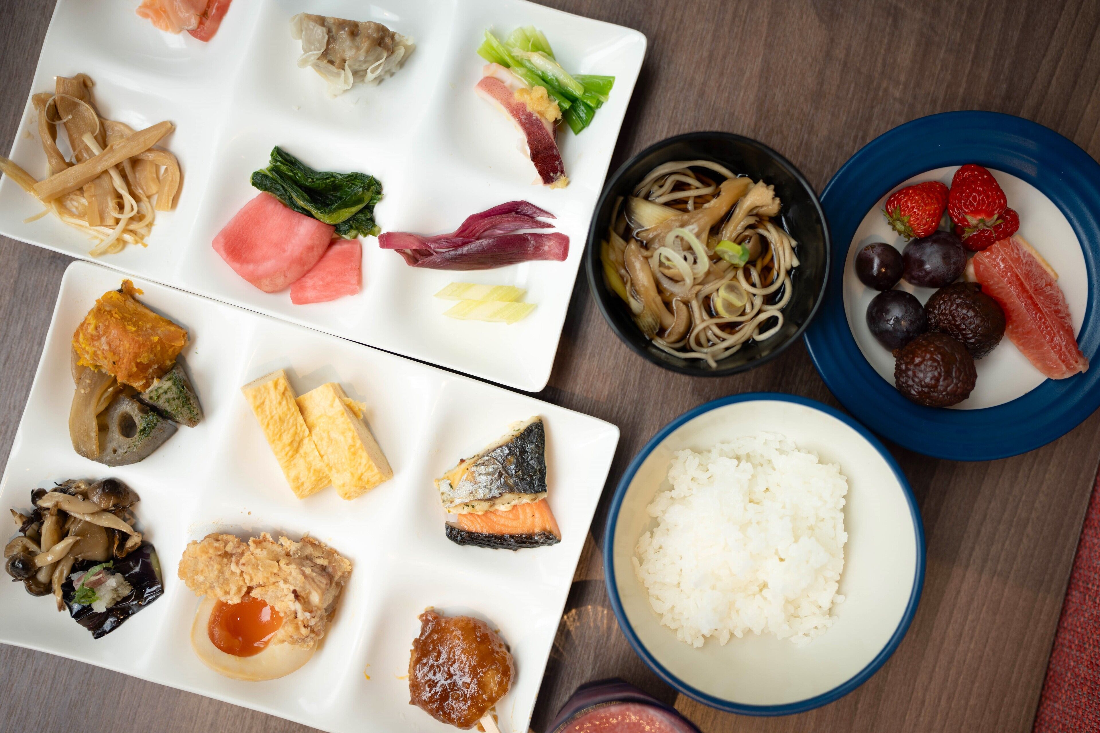 A variety of dishes including noodles, rice, and seafood, arranged on a wooden table.