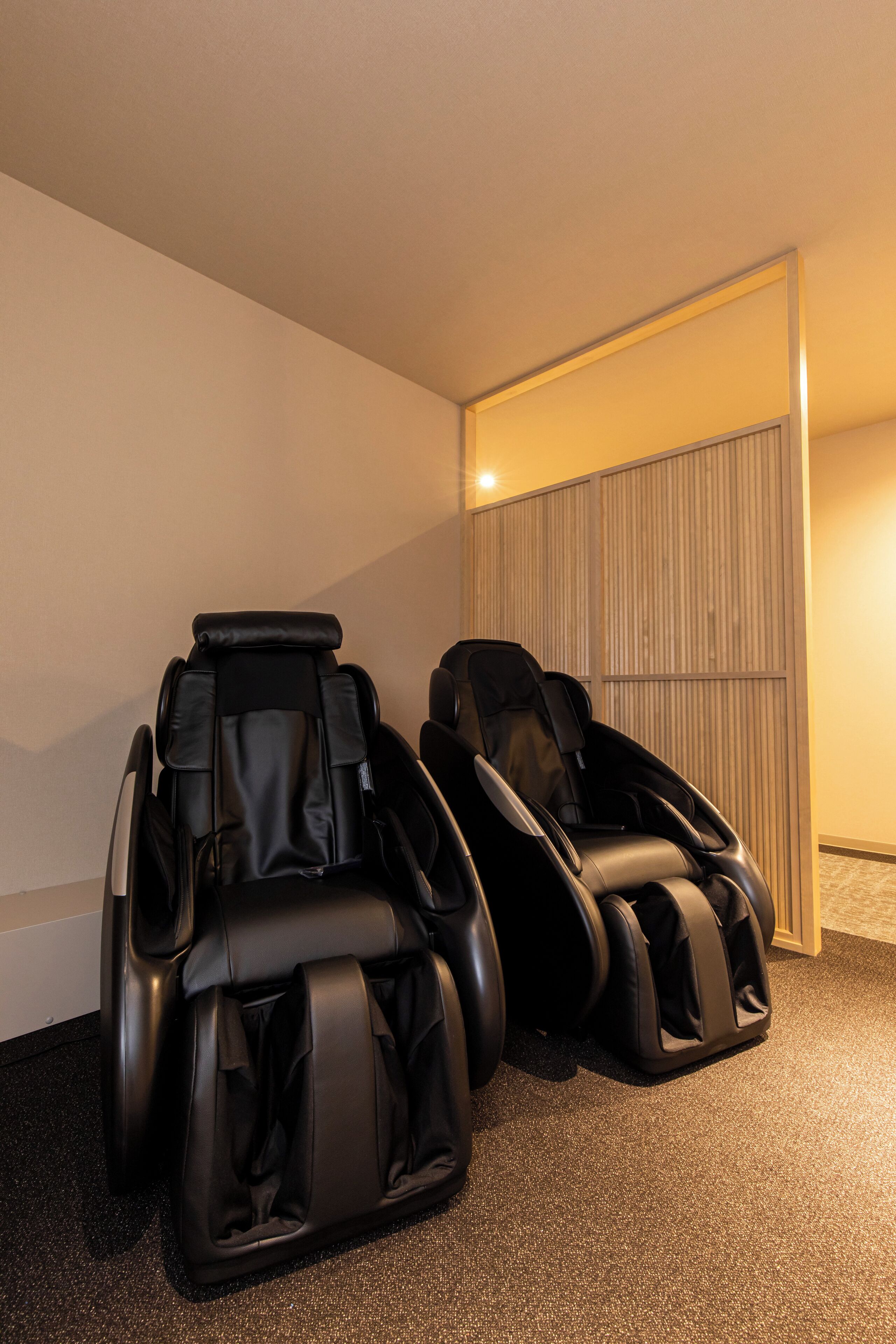 Two massage chairs in a room with a wooden panel wall and carpeted floor.