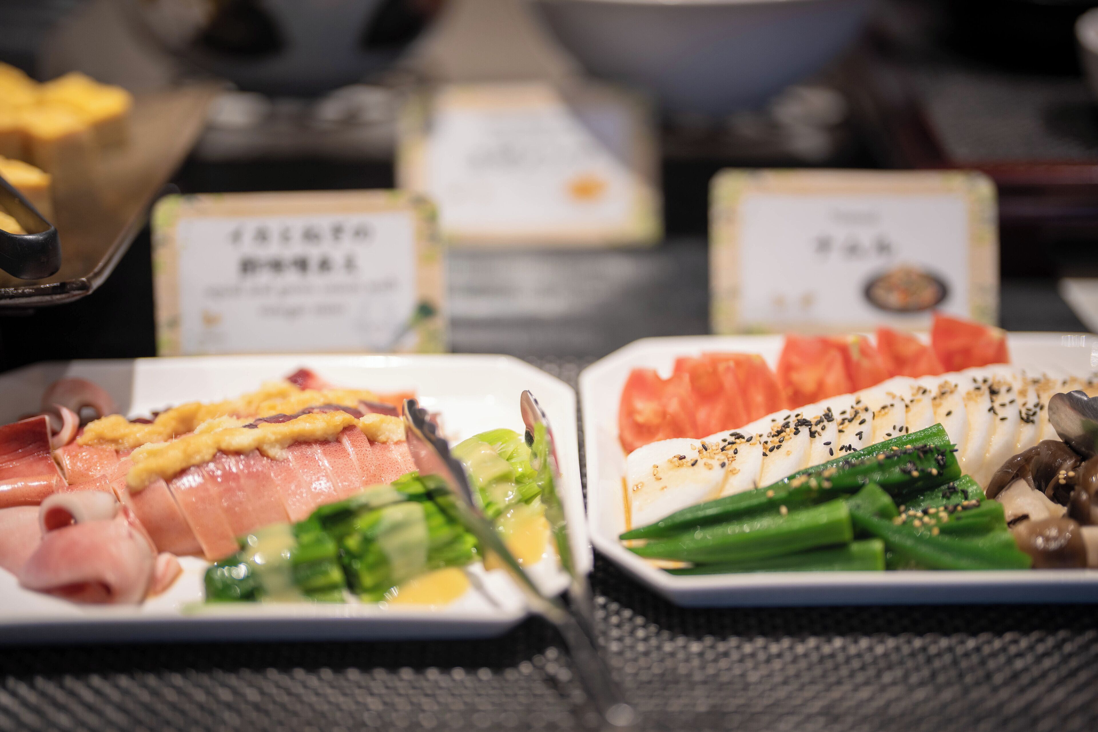 Una mesa con diversos platos, incluyendo sashimi y verduras, con etiquetas que identifican el tipo de comida.