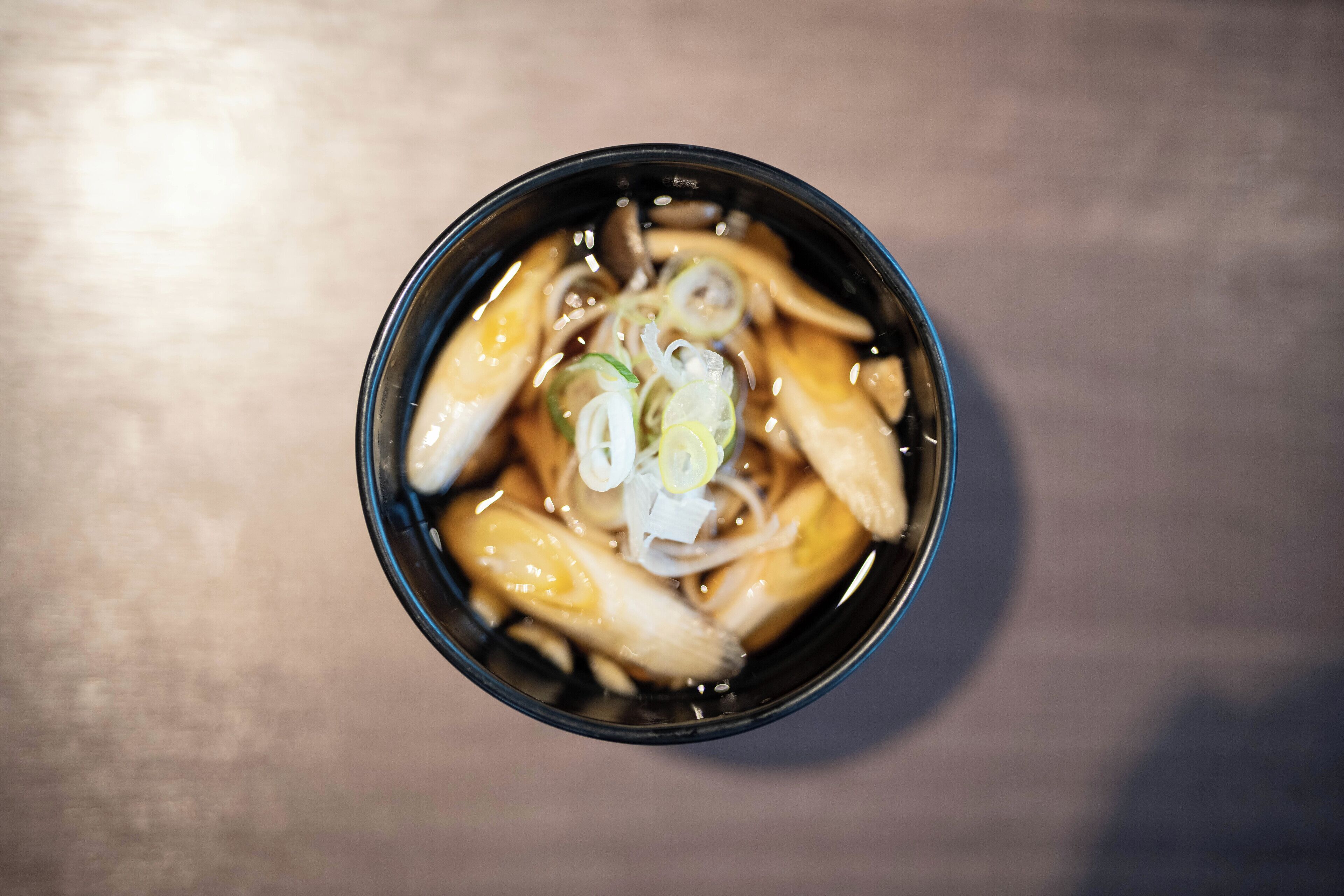 A bowl of soup with noodles and sliced green onions.