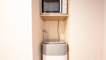 Une cuisine compacte avec un micro-ondes posé sur une étagère et un distributeur d’eau en dessous.