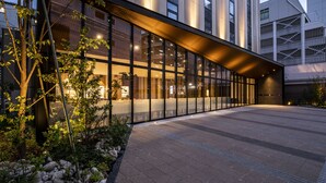 Un edificio moderno con amplios ventanales, techo curvo y un acceso pavimentado con rocas y plantas.