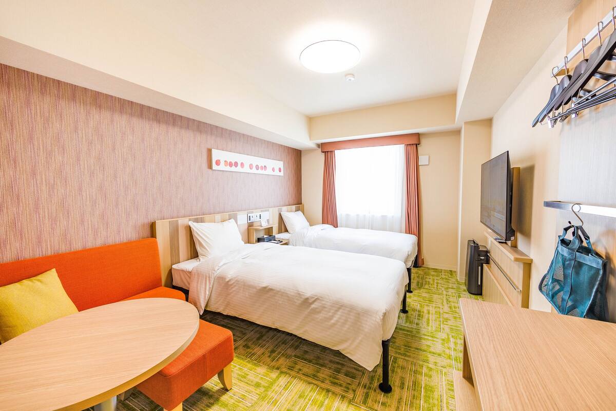 A hotel room with two beds, a sofa, a table, and a TV.