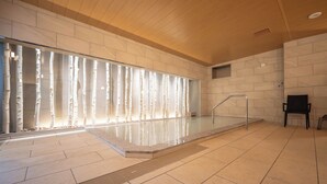Una piscina interior moderna con pared de vidrio, techo de madera y suelo de baldosas.