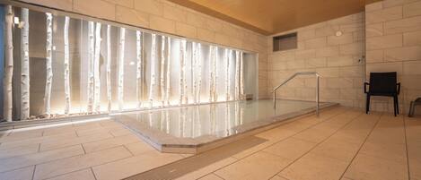 A modern indoor swimming pool with a glass wall, wooden ceiling, and tiled floor.