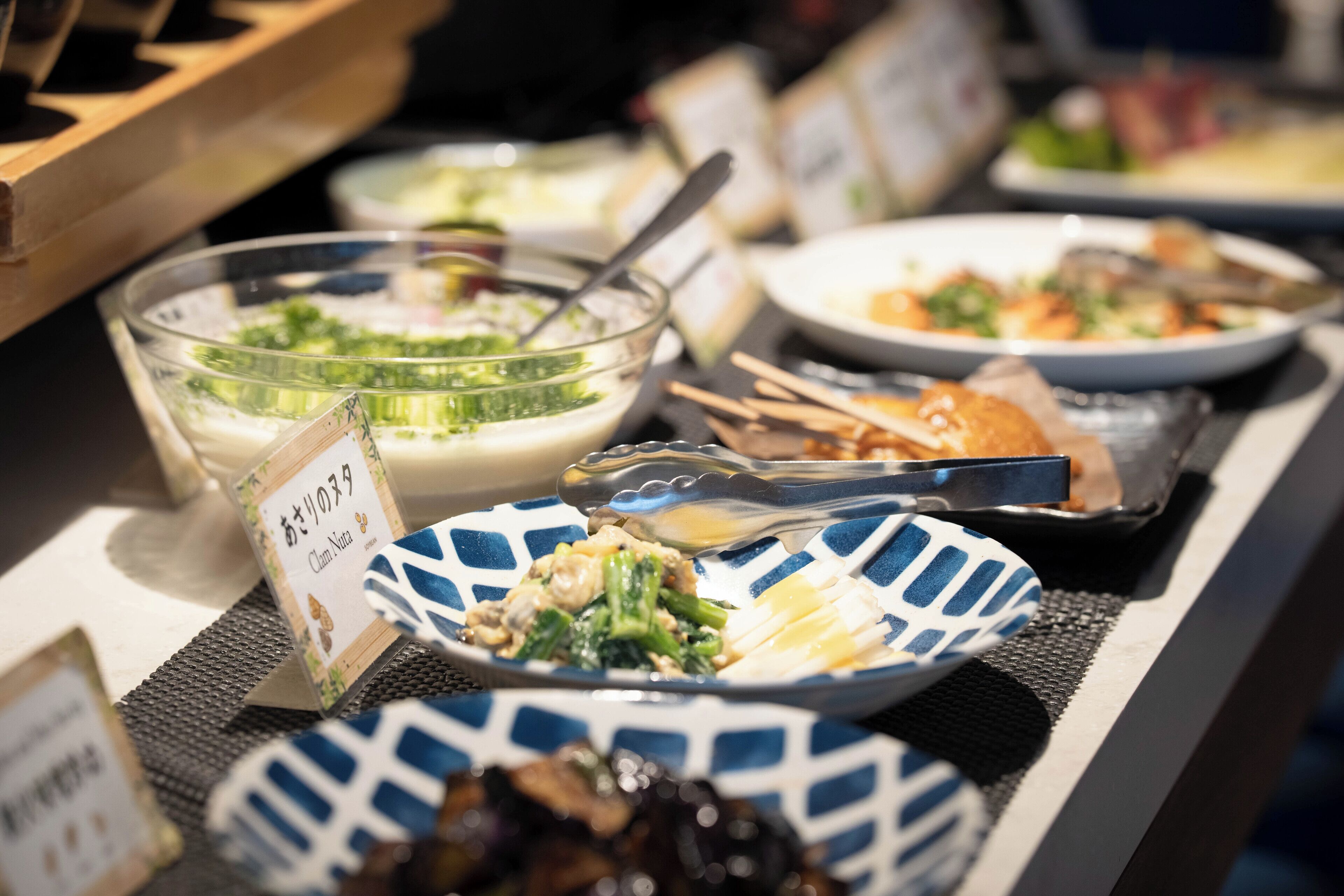 A buffet table with various dishes, including a bowl of salad, a plate of chicken, and a dish with a blue and white pattern.