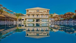 A multi-story hotel with a pool in the foreground, reflecting the building and surrounding structures. - Altura Hotel Zakynthos (Zakynthos)