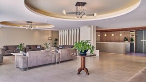 A modern living room with a sofa set, a round wooden coffee table, and a potted plant. - Altura Hotel Zakynthos (Zakynthos)