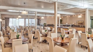 A spacious hotel dining area with multiple tables and chairs, large windows, and modern chandeliers. - Altura Hotel Zakynthos (Zakynthos)