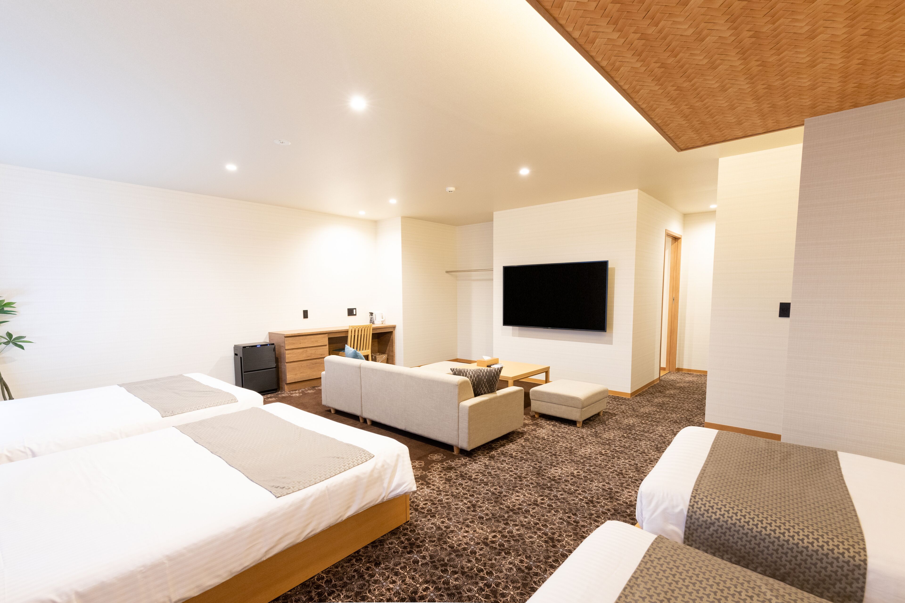 Ein modernes Hotelzimmer mit zwei Betten, einem Sofa, einem Schreibtisch und einem Fernseher.