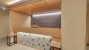 Ein moderner Hotelrezeptionstresen mit einer Holzschienkendecke, einer Wand mit dekorativer Gestaltung und einem strukturierten Glasschirm.