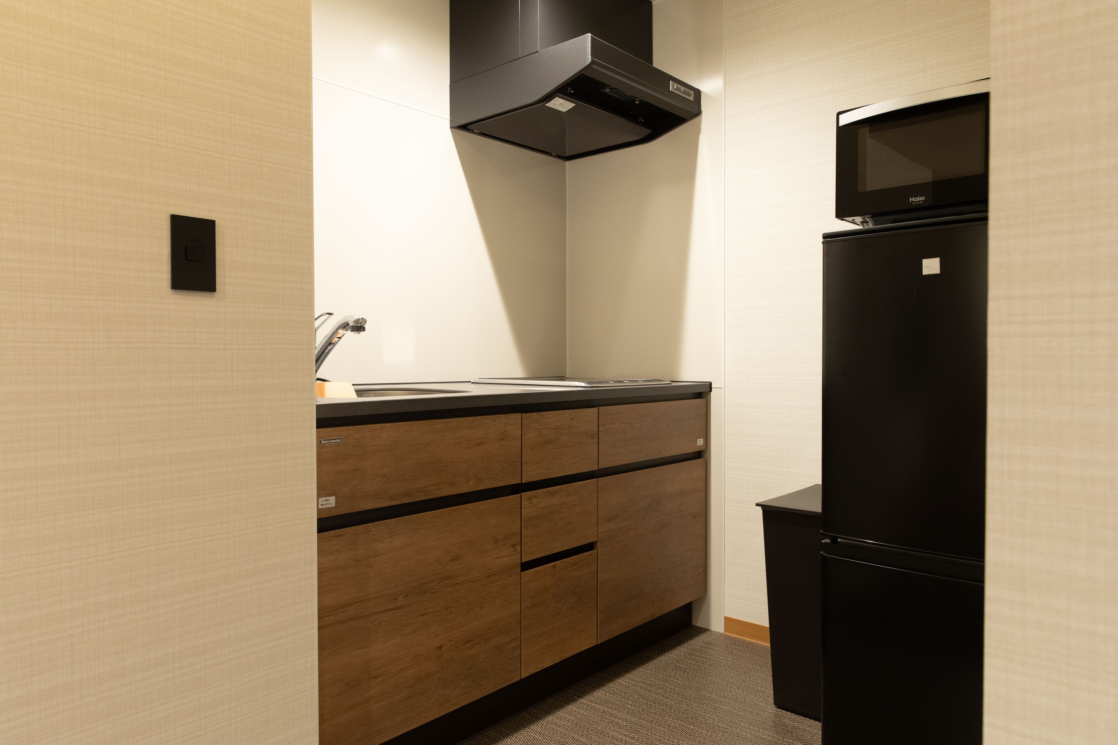 A compact kitchen with a black refrigerator, a microwave, and a wooden cabinet with drawers.