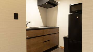 A compact kitchen with a black refrigerator, a microwave, and a wooden cabinet with drawers.