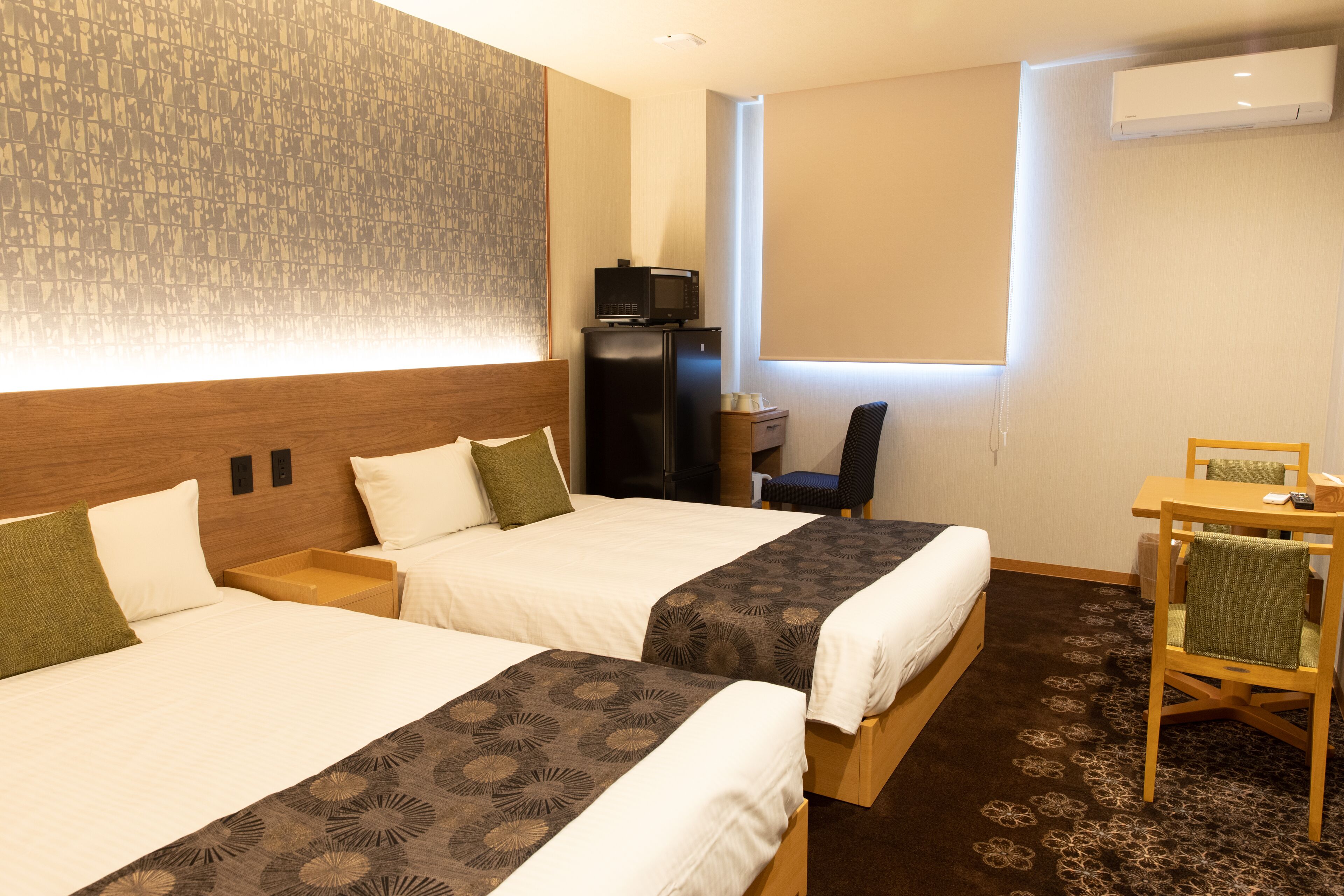 A hotel room with two beds, a desk with a computer, a chair, and an air conditioning unit.