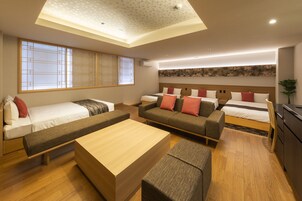 A modern hotel room with a large bed, a sofa, a bench, and a small table. There is a large window with a view of the outside.