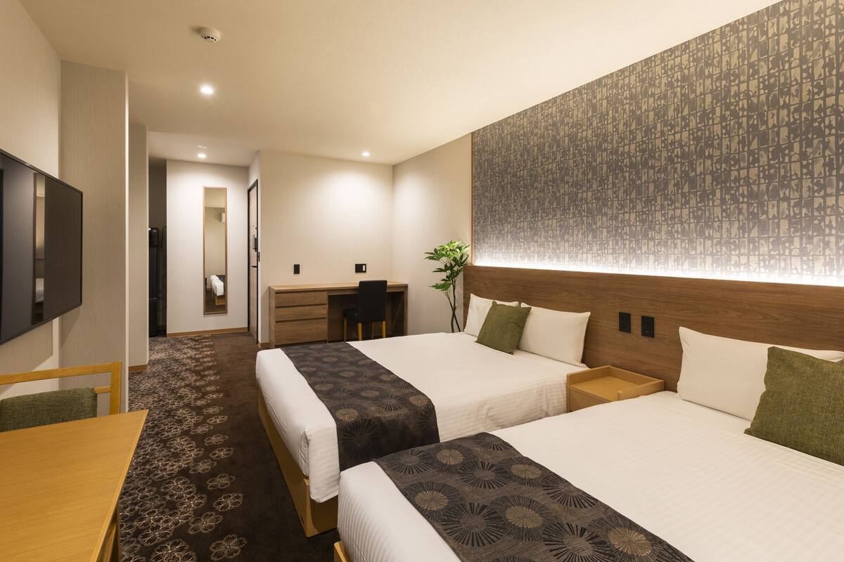 Une chambre d’hôtel avec deux lits, un bureau, une télévision et un mur décoré de motifs.