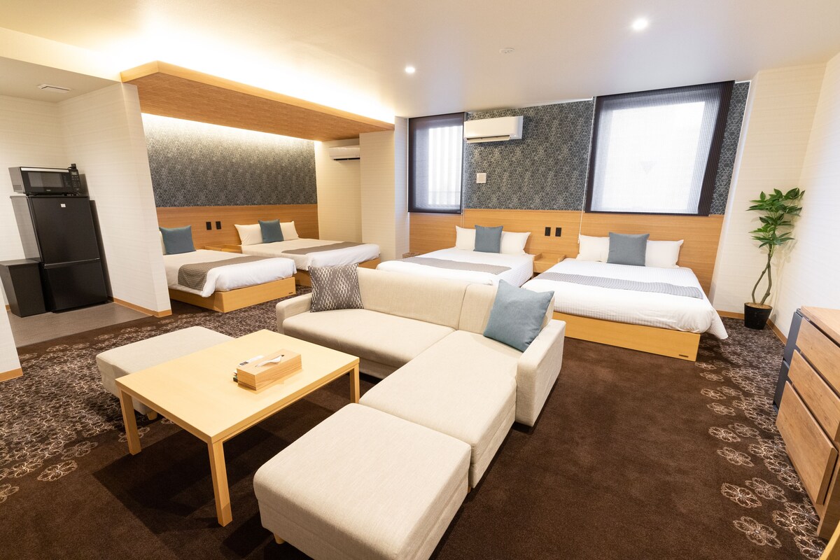 Ein Hotelzimmer mit zwei Betten, einem Schlafsofa, einem Couchtisch und einer kleinen Küchenzeile mit Kühlschrank und Mikrowelle.