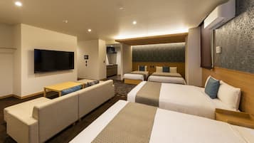 A hotel room with a flat-screen TV, a sofa, two beds with headboards, a wooden table, and a patterned wall.
