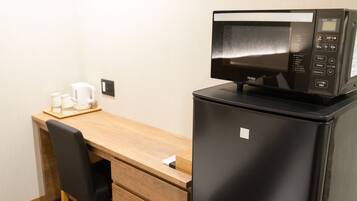 A compact hotel room with a wooden desk, a black refrigerator, and a microwave on top.