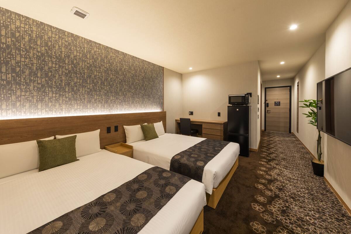 Une chambre d’hôtel avec deux lits, un bureau, une télévision et une moquette à motifs.