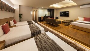 Ein modernes Hotelzimmer mit drei Betten, einer Couch, einem Fernseher und einer Küchenzeile.