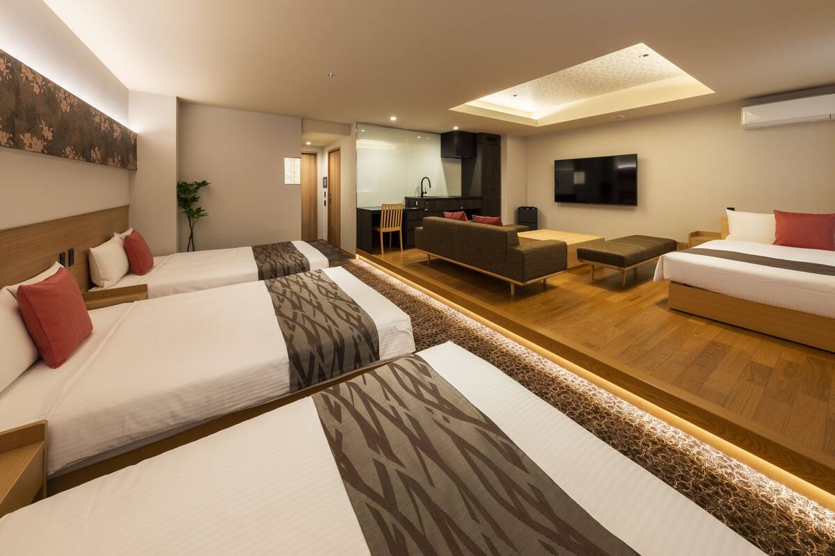 Une chambre d’hôtel moderne équipée de trois lits, d’un canapé, d’une télévision et d’une kitchenette.