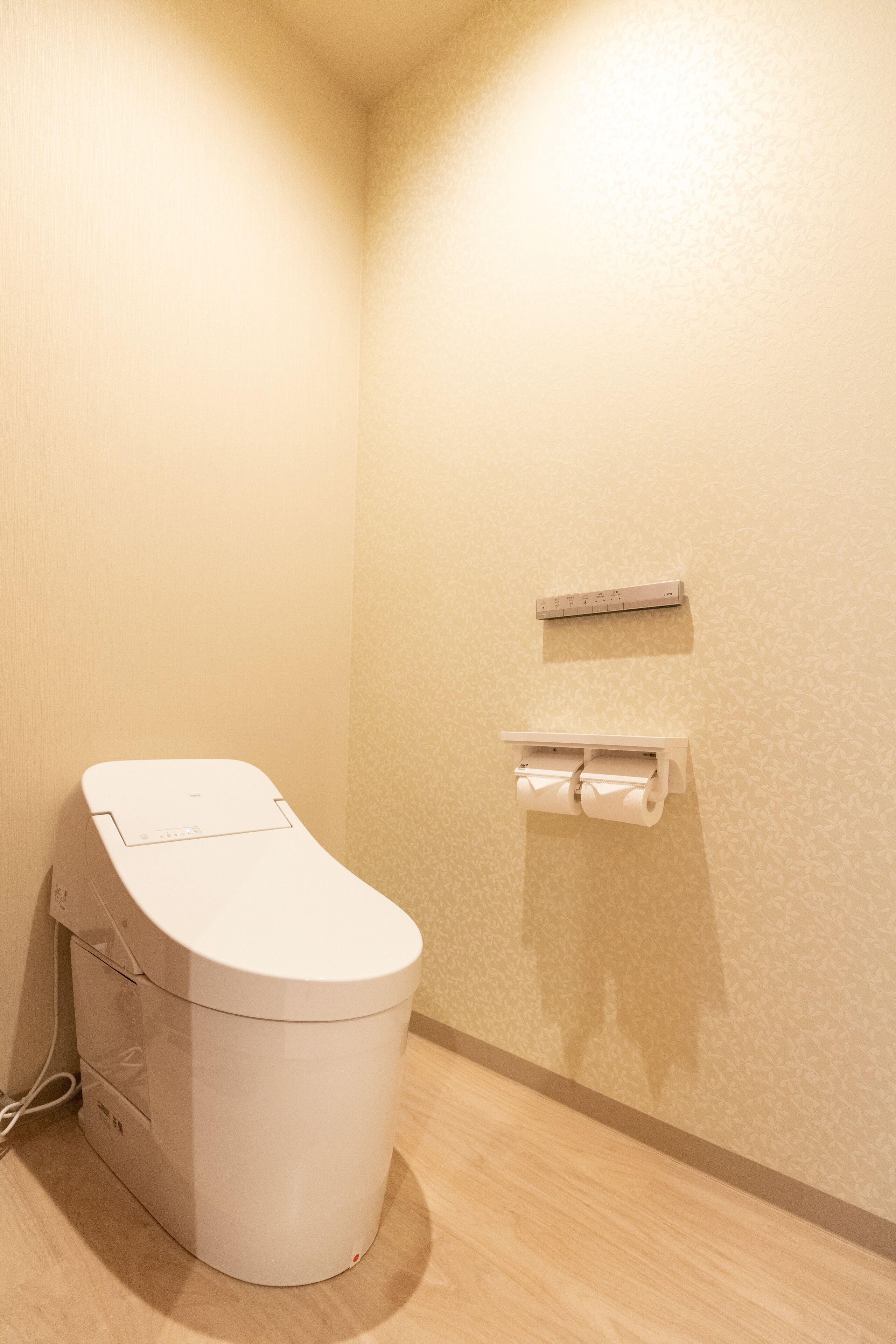 A small, modern bathroom with a toilet, a paper towel dispenser, and a power outlet on the wall.