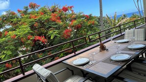 An outdoor dining area with a table set for four, surrounded by lush greenery and red flowers. - Peaceful Kona Retreat—Steps to Magic Sands Beach · Ocean View · King Beds · AC! (Kailua-Kona)
