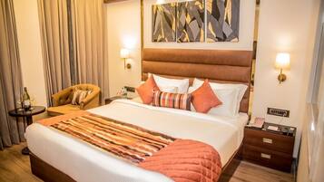 Quarto de hotel com cama grande, uma cadeira, mesa de cabeceira e uma obra de arte na parede.