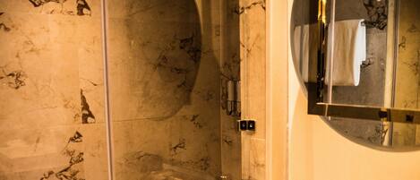 A modern bathroom with a glass-enclosed shower, a marble-tiled wall, and a large mirror above the sink.