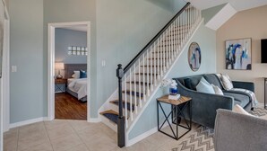 Un salon moderne avec un escalier, un canapé, une table basse et un tableau au mur.