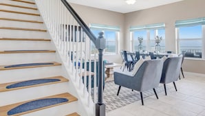 Un intérieur moderne avec un escalier, un coin repas et de grandes fenêtres.