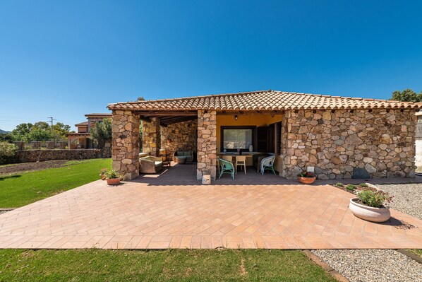 Un bâtiment en pierre avec un toit en tuiles, un patio aménagé avec des chaises et des tables, et une vue sur le paysage environnant.
