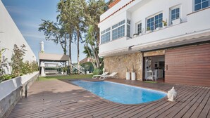 A swimming pool with a wooden deck, a white building with a stone facade, and a clear sky. - "Loft la Matanza" with Sea View, Mountain View, Pool, Terrace & Garden (La Matanza)