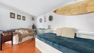 A room with a bed, a pool table, a sofa, and a surfboard on the wall.