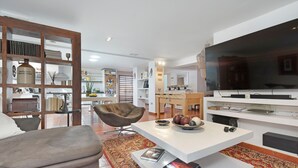 A modern living room with a sofa, coffee table, TV, bookshelf, and dining area. - "Loft la Matanza" with Sea View, Mountain View, Pool, Terrace & Garden (La Matanza)