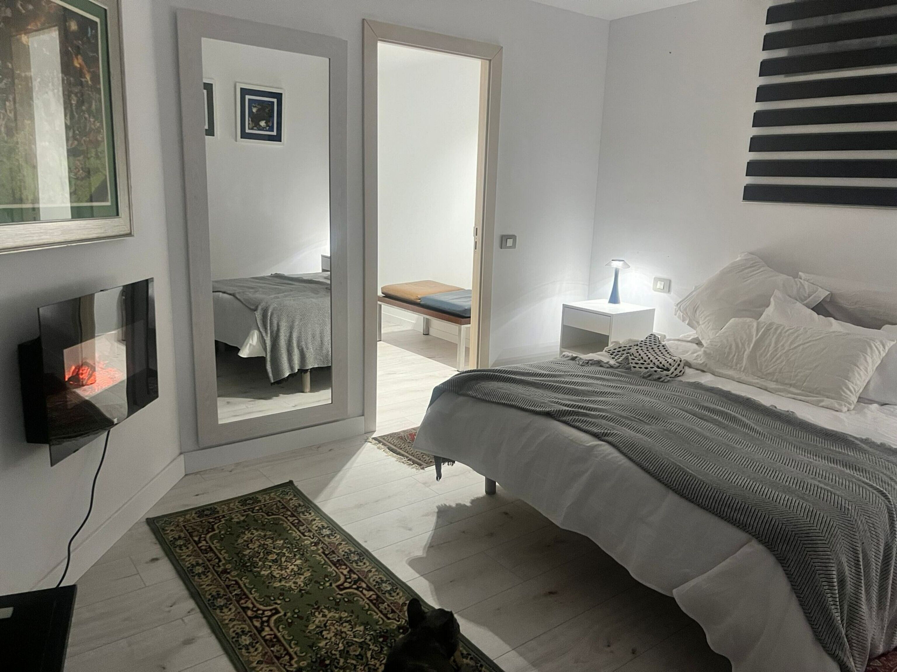 A bedroom with a bed, bedside table, lamp, and a TV mounted on the wall.