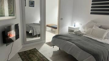 A bedroom with a bed, bedside table, lamp, and a TV mounted on the wall.