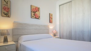Un dormitorio con cama, mesita de noche, lámpara y dos cuadros colgados en la pared.