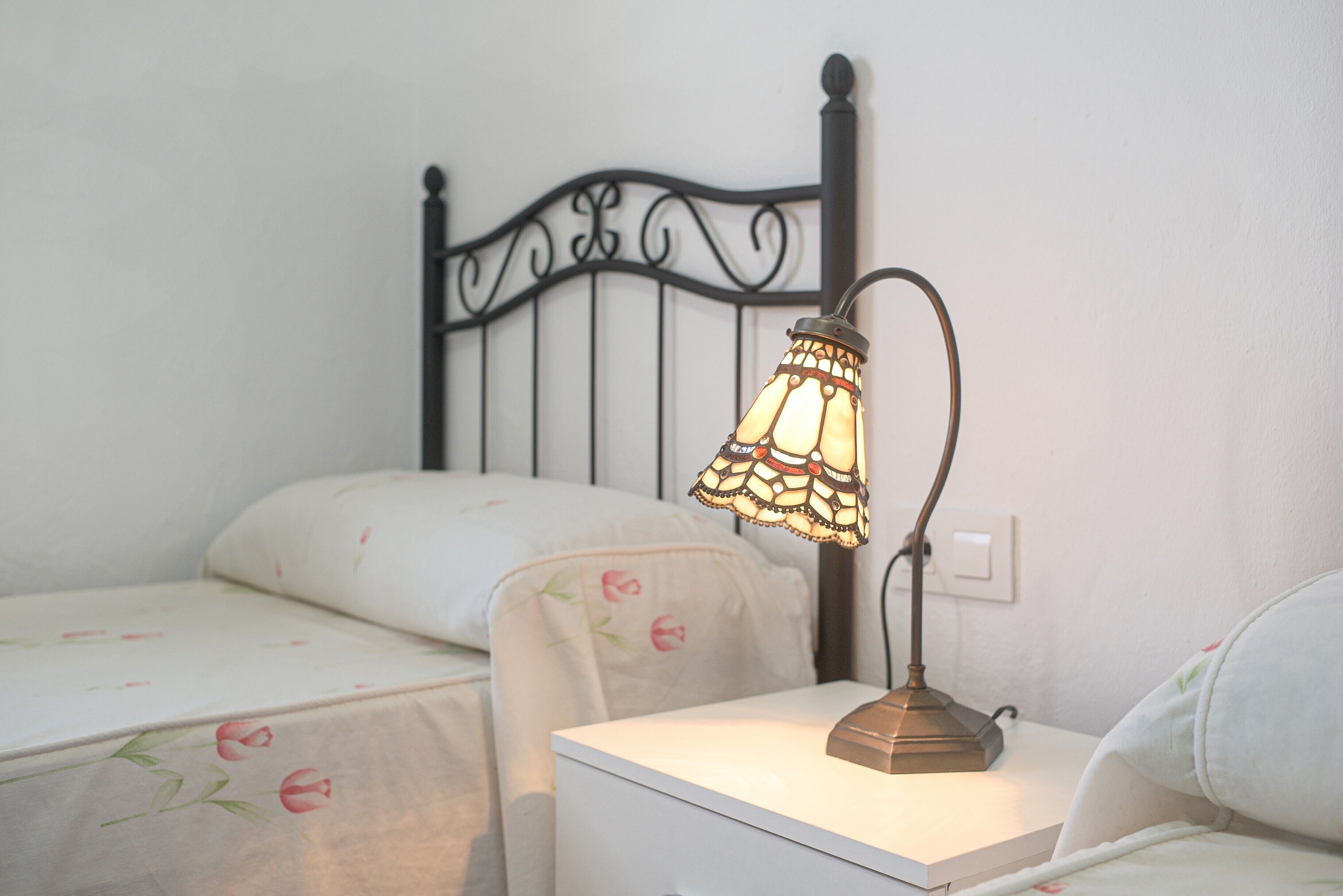 A bed with a metal headboard, a bedside table with a lamp, and a floral-patterned bedspread.