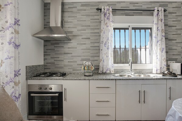 Una cocina moderna con estufa a gas, horno, armarios de acero inoxidable y una ventana con cortinas.