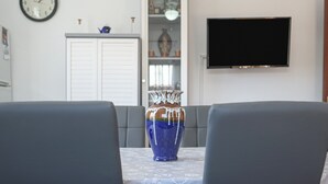 Un comedor con una mesa, sillas, un jarrón, un reloj, un armario y un televisor.
