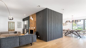 Una sala de estar moderna con un sofá seccional gris, una chimenea y un comedor con un ventanal grande.