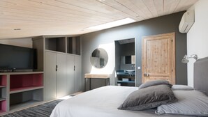 Un dormitorio con cama, televisor, armario, espejo y baño.