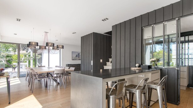 Una cocina moderna con una isla central, taburetes de bar y una zona de comedor con mesa y sillas.